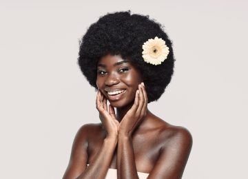 Portrait of beautiful young African woman touching face and smiling while standing against gray background