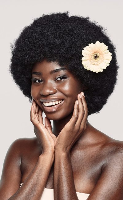 Portrait of beautiful young African woman touching face and smiling while standing against gray background