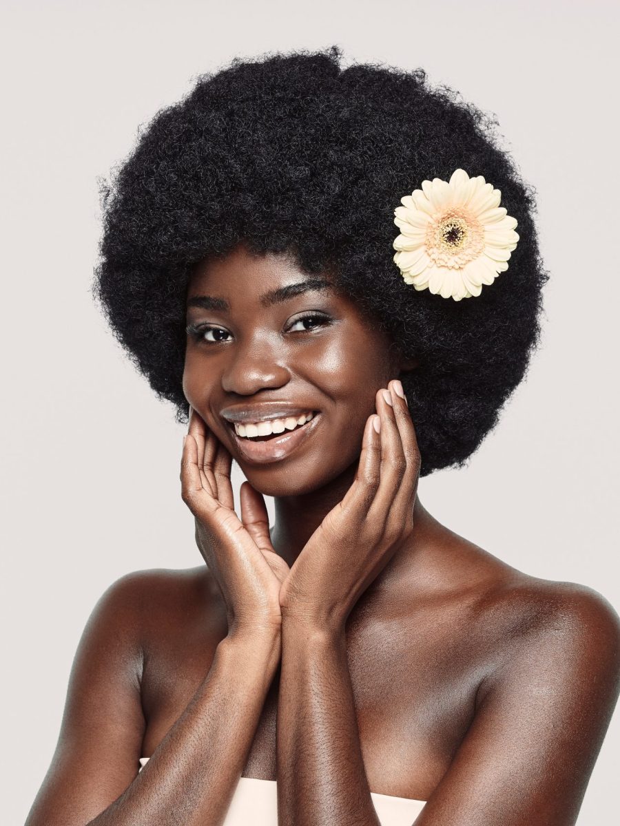 Portrait of beautiful young African woman touching face and smiling while standing against gray background